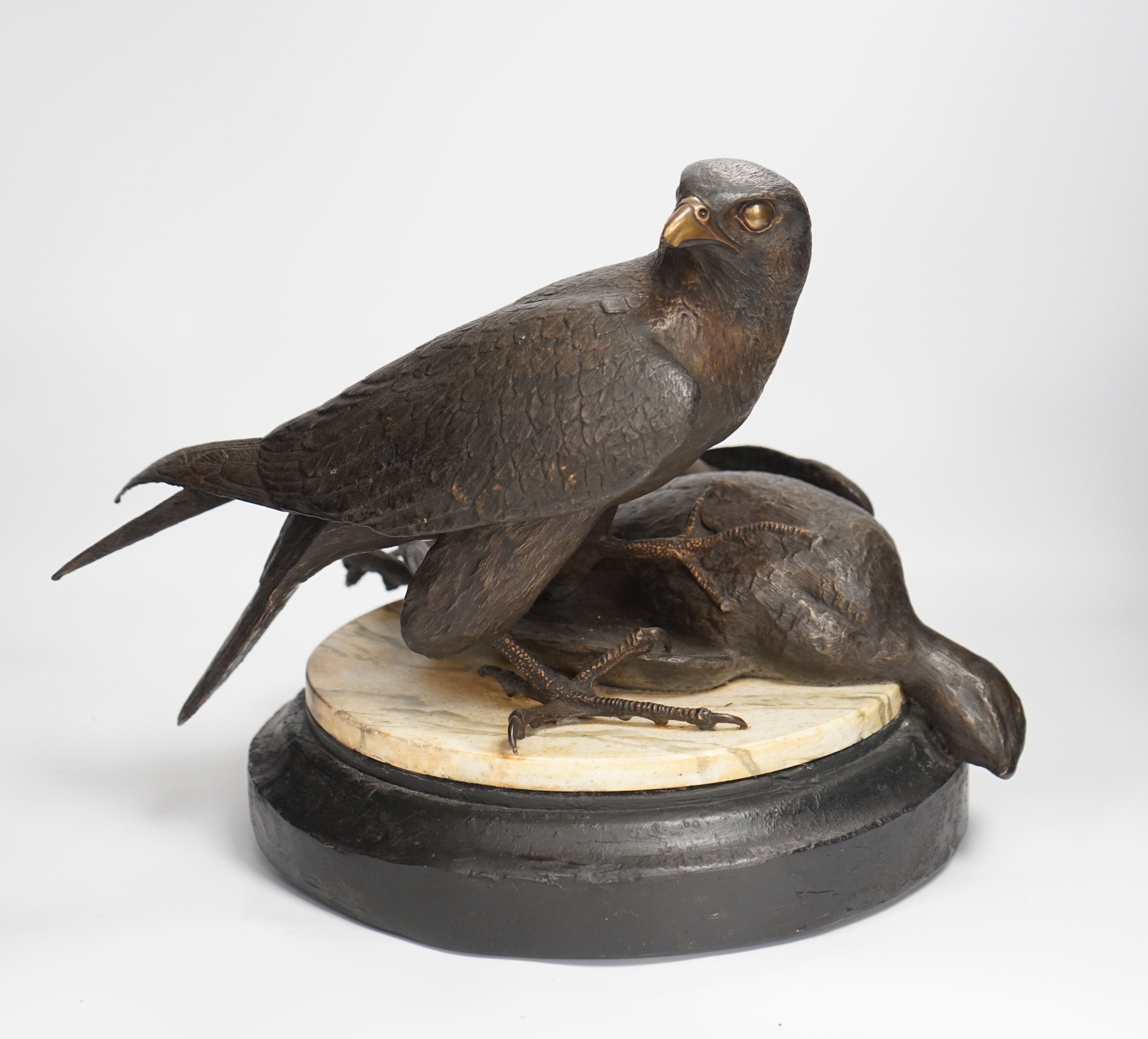 A limited edition bronze bird of prey with a kill, on a faux marble disc and painted wooden stand, 29cm high